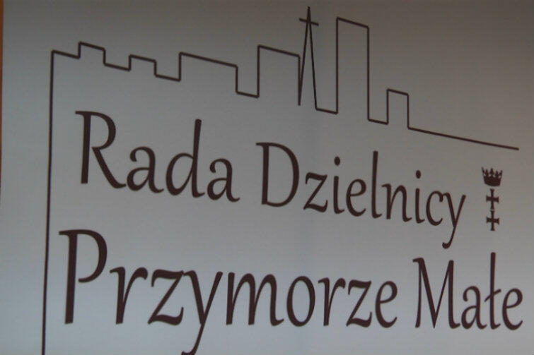 Tablica wskazująca siedzibę Rady Dzielnicy Przymorze Małe w udany sposób podkreśla urbanistyczny charakter tej części Gdańska - blokowisko z charakterystyczną wieżą kościoła NMP Królowej Różańca Świętego (tzw. Okrąglak).