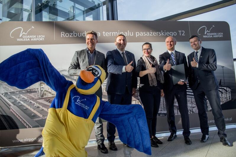 Umowa na budowę pirsu terminala T2. Nz. od lewej Tomasz Kloskowski - prezes Portu Lotniczego Gdańsk, Piotr Borawski - zastępca prezydenta Gdańska ds. przedsiębiorczości i ochrony klimatu, Aleksandra Dulkiewicz - prezydent Gdańska oraz Karol Zduńczyk prezes DORACO i Radosław Preiss członek Zarządu DORACO. Z przodu mewa - maskotka gdańskiego Portu Lotniczego