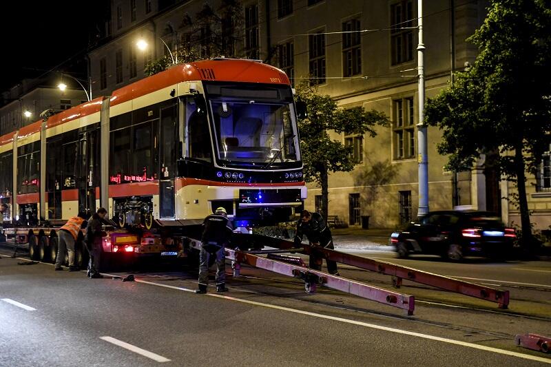 Noc, czterech mężczyzn w roboczych ubraniach ściąga po specjalnych szynach tramwaj na tory