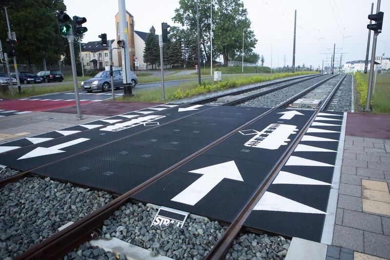 Na zdjęciu widać tory tramwajowe, w części otoczonej czarnym gumowym chodnikiem z białymi piktogramami tramwaju
