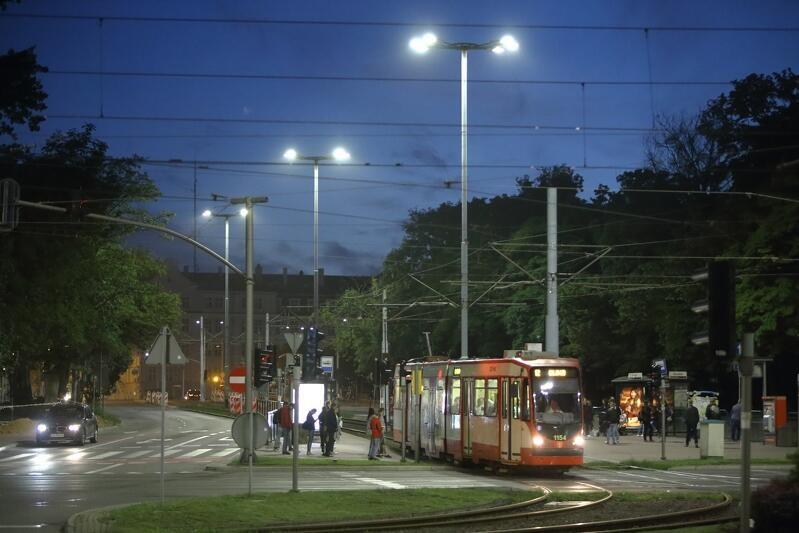 tramwaj w nocy przy skrzyżowaniu Hucisko w Gdańsku, piesi przechodzą przez przejście przed tramwajem stojącym na światłach
