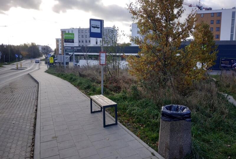 Ulica i przystanek autobusowy, na którym stoi ławka, po prawej stronie - kosz na śmieci