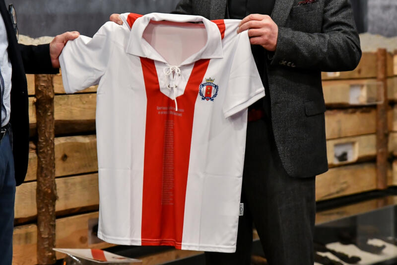 Na zdjęciu okolicznościowa koszulka piłkarska GKS Gedania 1922. W środku koszulki podłużny czerwony pas, boki i rękawy są białe.