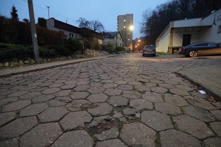 Na zdjęciu fragment ulicy wykonany z betonowych płytek, w tle widać kilka samochodów osobowych