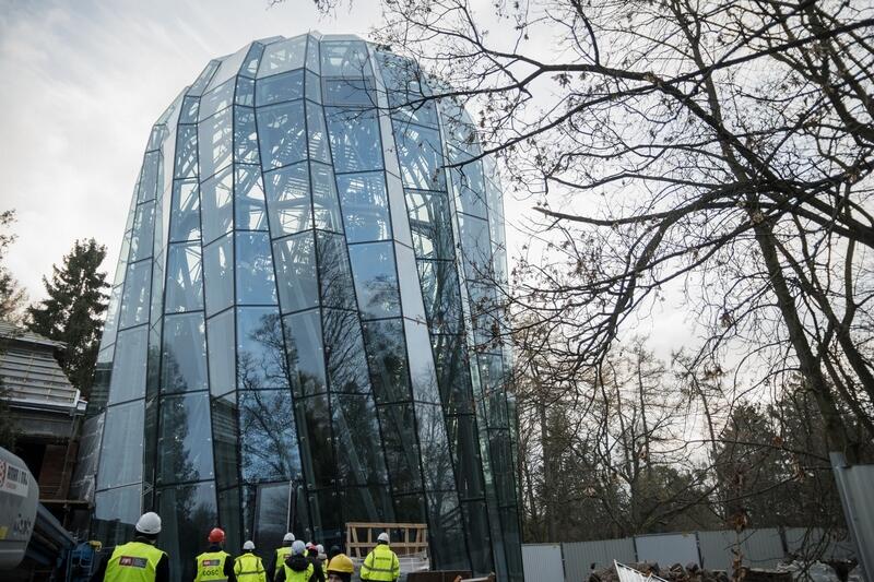 Wysoka, kilkunastometrowa budowa ze szkła z półkolistą górą. Na dole stoi kilka osób w hełmach