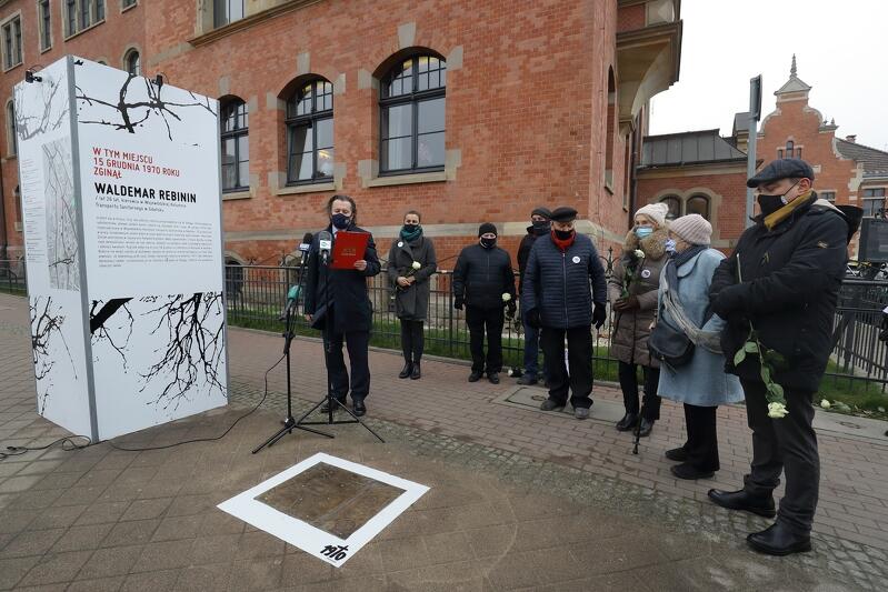 grupa osób w zimowych ubraniach stojąca nad płytą umieszczoną w chodniku