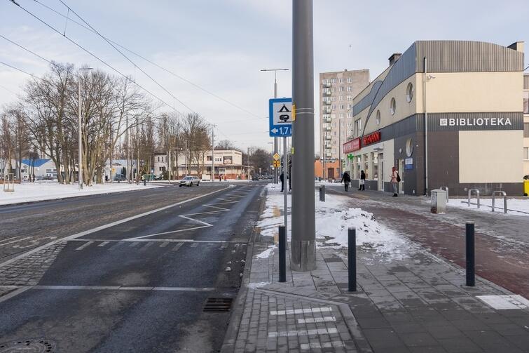 na zdjęciu widać wyniesienie wybudowane w jezdni, to element przystanku komunikacji miejskiej. W tle po rawej stronie widać jasne budynki mieszkaniowe