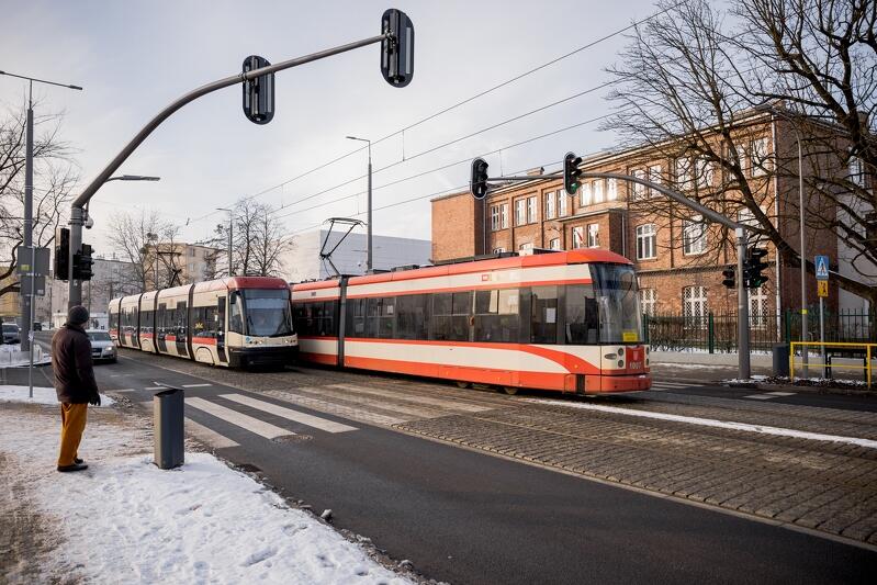 na zdjęciu widać dwa kremowo-czerwone tramwaje, wymijające się na przeciwległych torach, w tle za nimi kamienica z ciemnoczerwonej cegły