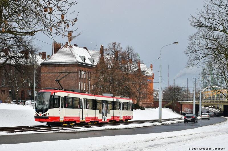 biało czerwony tramwaj na torach, przy nim ulica, śnieg