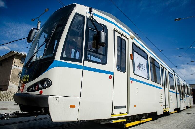 perłowo biały tramwaj z wąskimi niebieskimi paskami nad i pod oknami
