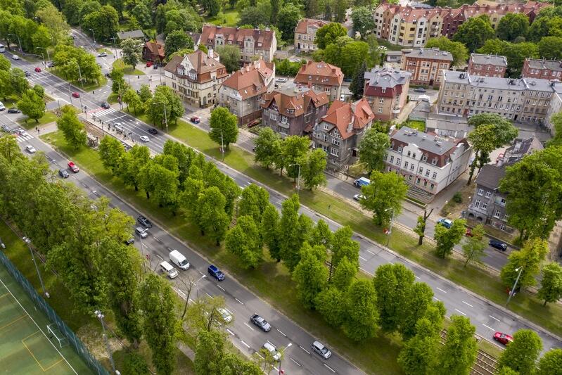 zdjęcie wykonane z lotu ptaka, widać na nim dwie jezdnie trzypasmowe i jedną dwupasmową, jadą nimi samochody osobowe, jezdnie rozdzielają zielone szpalery drzew z trawnikami, po prawej widać kilka zabytkowych kamienic