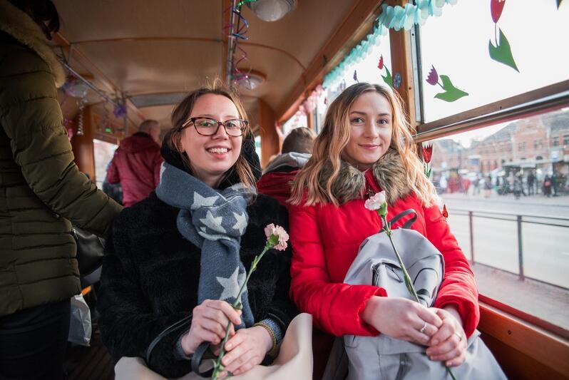 dwie młode dziewczyny z goździkami w ręku na pokładzie zabytkowego tramwaju