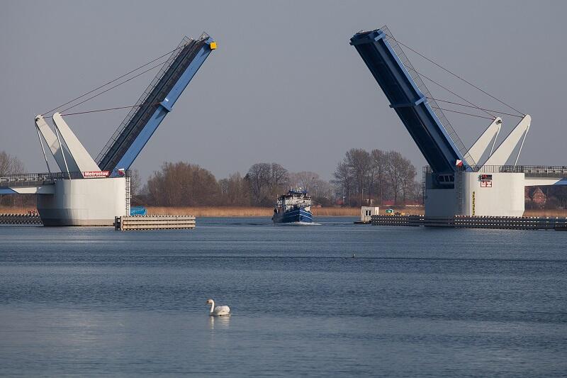 otwarty most pod którym przepływa kuter, na pierwszym planie, przed mostem łabędź
