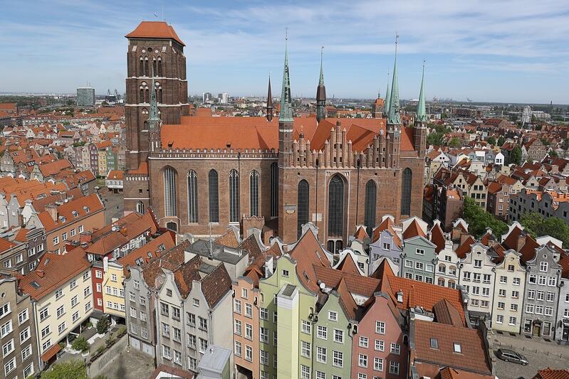 Panorama Bazyliki Mariackiej, widocznej w słońcu, pośród kamienic Głównego Miasta. Zdjęcie wykonane ze szczytu wieży Ratusza Głównomiejskiego