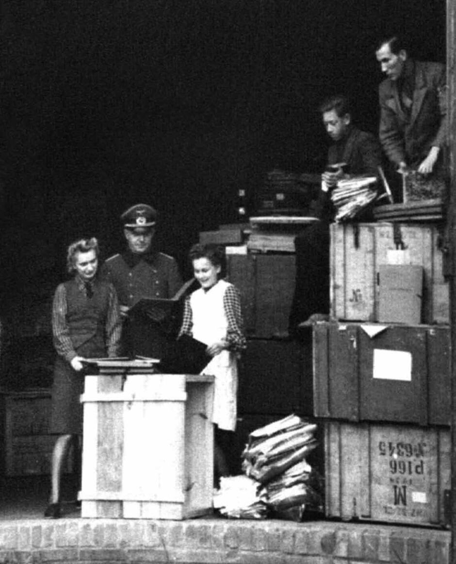 Niemiecki oficer w towarzystwie personelu pomocniczego przegląda zbiory zgromadzone w archiwum