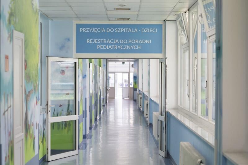 Szklane drzwi z napisem "Rejestracja do poradni pediatrycznych", za nimi pusty korytarz szpitalny 