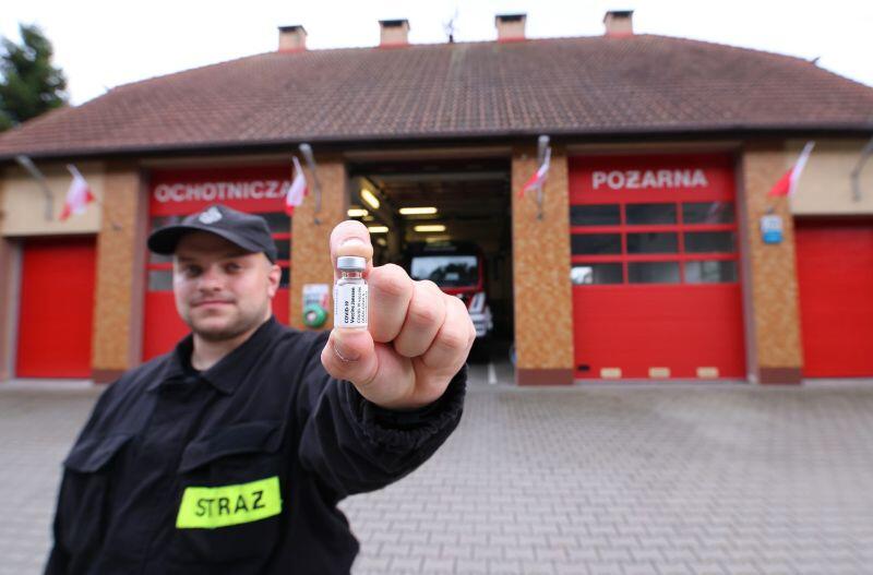 Dh Paweł Jackiewicz prezentuje fiolkę od szczepionki J&J przed strażnicą OSP Gdańsk Świbno