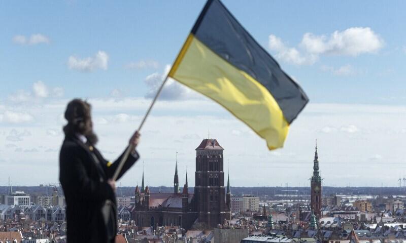 mężczyzna powiewa flagą czarno-żółtą, w tle widok na Gdańsk 