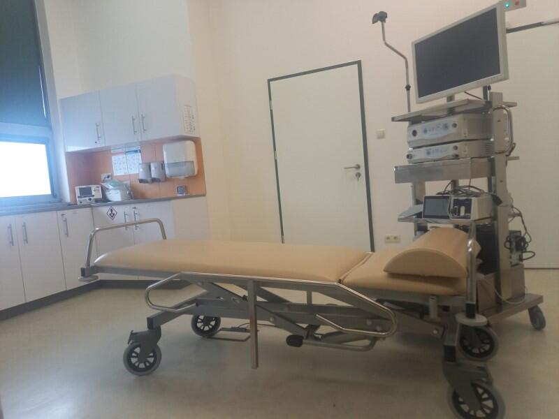Sala zabiegowa, po środku łóżko medyczne, po bokach sprzęt medyczny