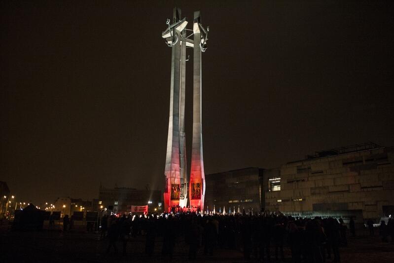 Trzy krzyże z kotwicami, Pomnik Poległych Stoczniowców 1970, wieczór, przed pomnikeim stoi kilkadziesiąt osób