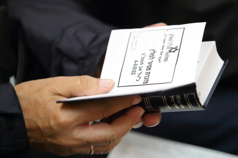 Zdjęcie przedstawia niewielką książkę rozłożoną w dłoniach mężczyzny - w zbliżeniu. Na wewnętrznej karcie książki znajduje się znak Gwiazdy Dawida i hebrajskie napisy 