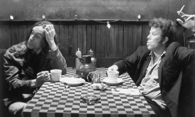 dwaj mężczyźni siedzą przy stoliku w kawiarni, palą papierosy