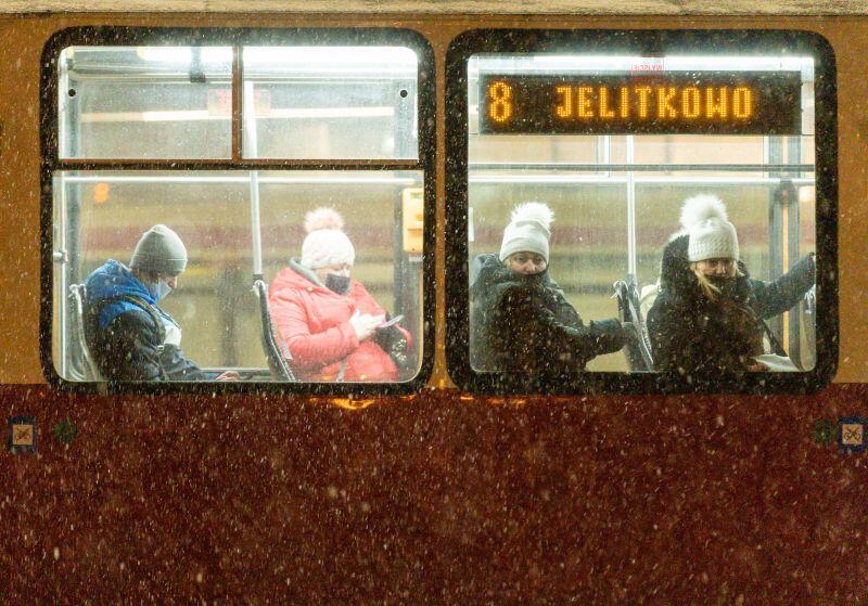 Kobiety w zimowych obrania siedzą w tramwaju, napis na tablicy świetlenej "Jelitkowo", na zewnątrz pada śnieg