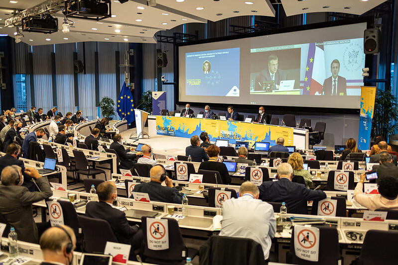 147e session plénière du Comité régional européen.  A l'écran (à droite) Emmanuel Macron, à côté d'Apostolos Tzitzikostas, président du Comité pour la Région Europe 