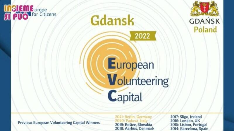 Tablica z informacją w języku angielskim, że Europejską Stolicą Wolontariatu na rok 2022 został Gdańsk. Po prawej w górnym rogu umieszczono herb Gdańska z lwami