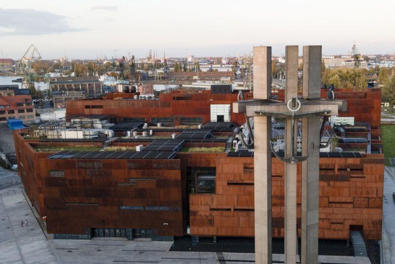 Pomnik Poległych Stoczniowców na Pl. Solidarności w Gdańsku na tle nowoczesnego budynku i stoczni