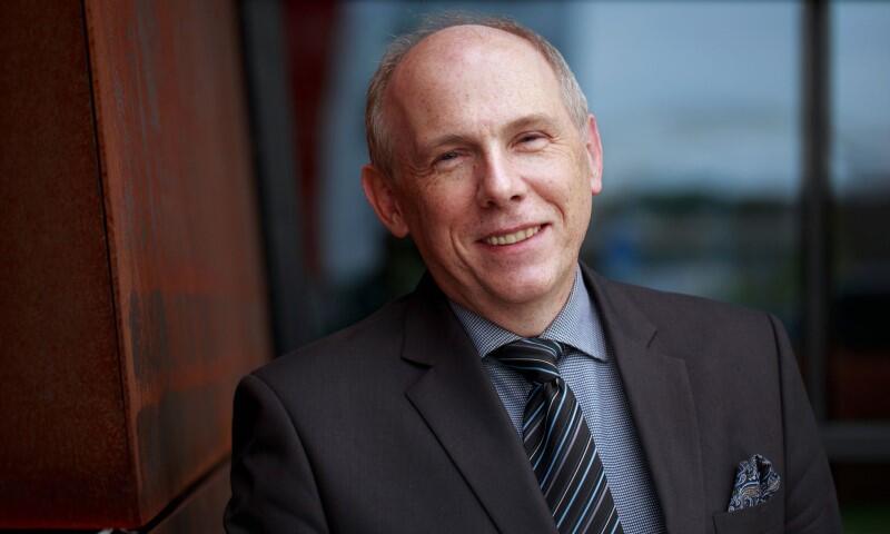 Portret uśmiechniętego mężczyzna w średnim wieku, ubrany jest w garnitur z poszetką 