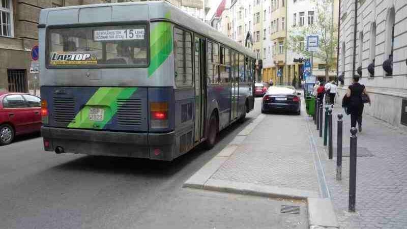 Miejska ulica. Widzimy od tyłu szaro-zielony autobus, który zatrzymał się przy antyzatoce. Antyzatoka jest po prawej stronie zdjęcia