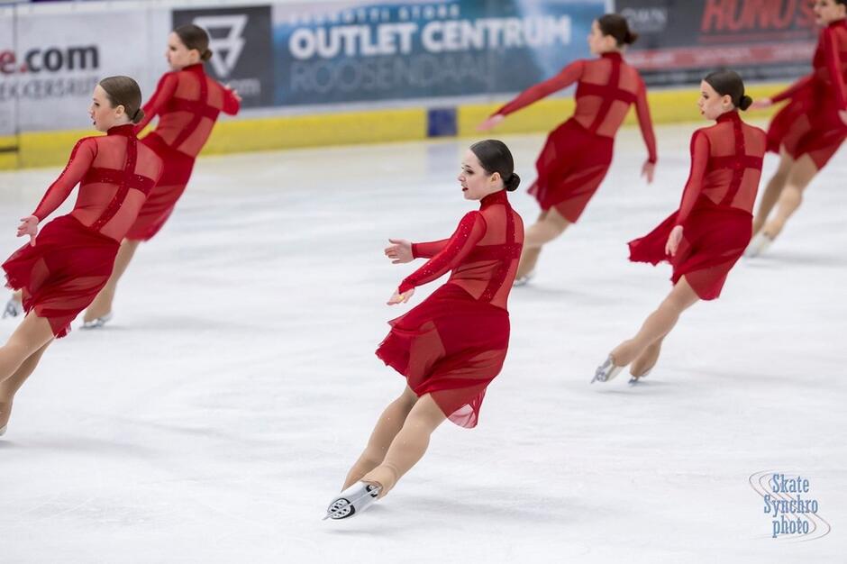 Sześć kobiet w czerwonych sukniach w łyżwach na lodzie
