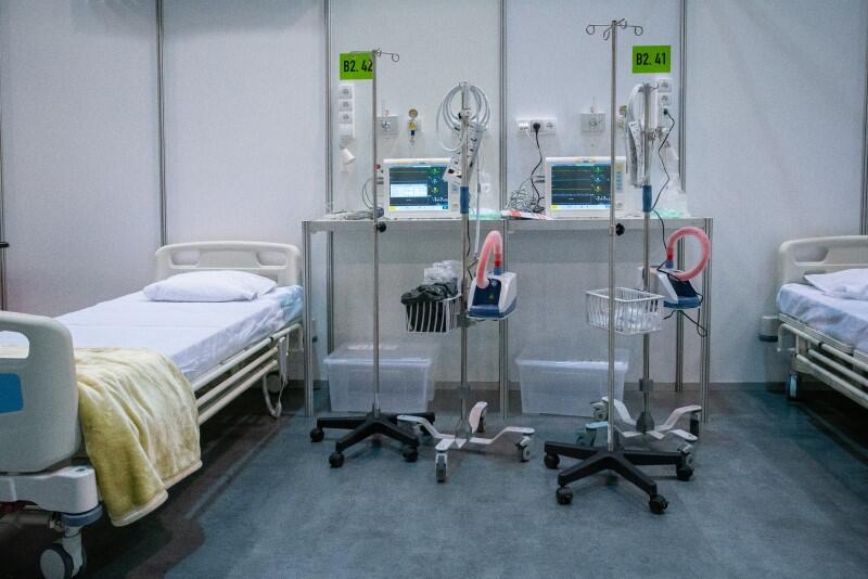 Po lewej szpitalne łózko obok stolik ze sprzętem medycznym 