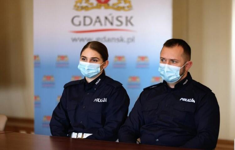 kobieta i mężczyzna w mundurach policyjnych, siedzą za stołem, mają maski na twarzach