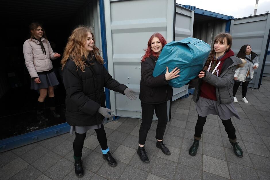 Harcerki ze Związku Harcerstwa Rzeczpospolitej wypakowują dary z norweskiego transportu do kontenerów magazynowych, które stoją przy stadionie