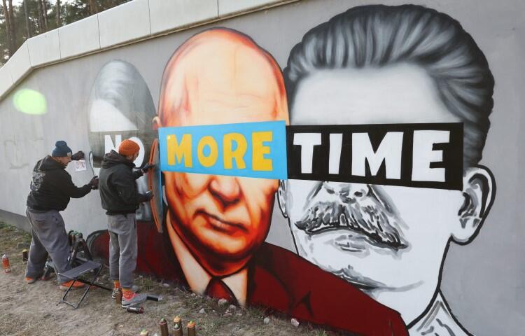 dwaj mężczyźni malują na ścianie mural: trzy głowy - Hitlera, Putina, Stalina z opaską na oczach z napisem: no more time