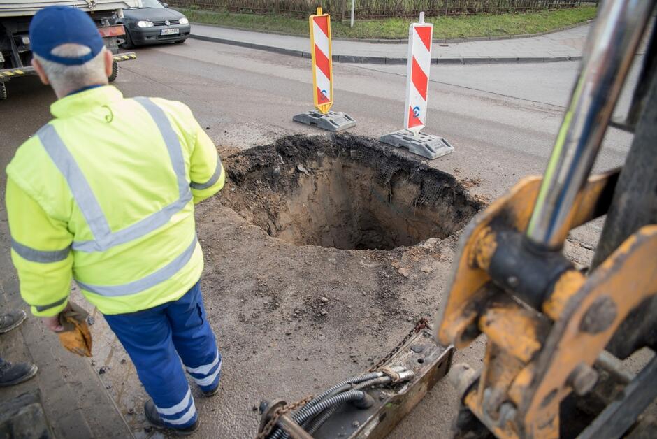 mężczyzna w ubraniu roboczym stoi nad otworem w jezdni