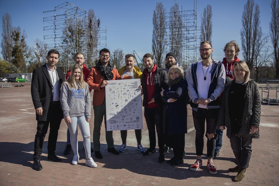 Gdańsk, Plac Zebrań Ludowych. Grupa osób stojącch koło siebie, dwóch mężczyzn trzyma plakat promujący Juwenalia