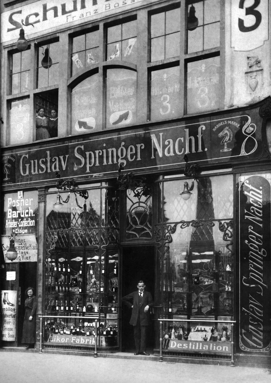 Przed głównym sklepem i biurem firmy na Targu Drzewnym; na szyldzie znak firmowy, którym od pewnego momentu był konik szachowy; około 1915