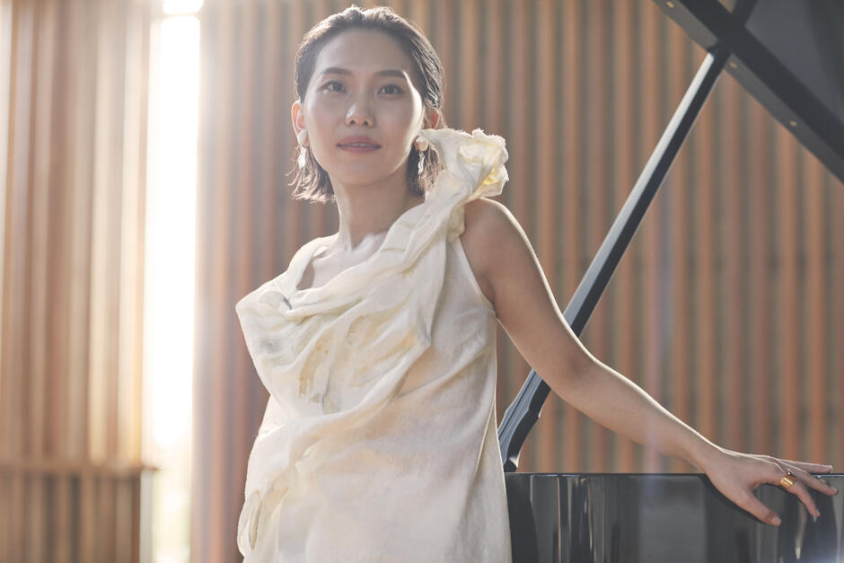 młoda kobieta ubrana w białą suknię, stojąca obok czarnego fortepianu