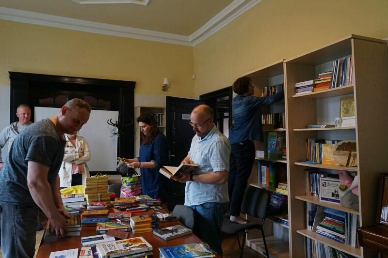 Stół z książkami, wokół niego stoi kilka osób, układa książki 