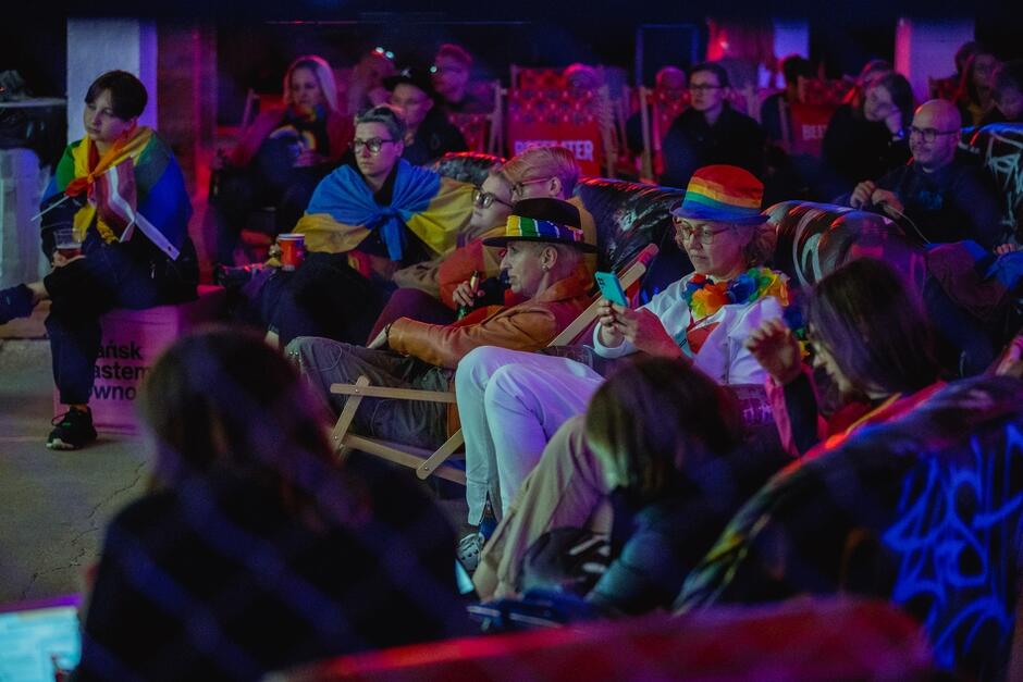 Kilka osób w kolorowych kapeluszach, siedzi na kanapach, leżakach 