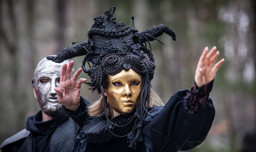 aktorzy w kreacjach teatralnych, mają czarne stroje i maski na twarzach 
