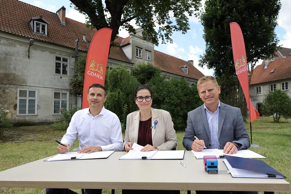 Aleksandra Dulkiewicz prezydent Gdańska (w środku) i Karol Kalinowski dyrektor DRMG (z prawej) oraz Stanisław Poniewierka, prezes zarządu firmy Poleko (z lewej) podpisują umowę na remont Zespołu Sierocińca