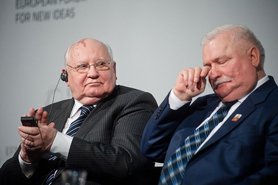 Po lewej siedzi Michaił Gorbaczow, przypatruje się Lechowi Wałęsie, który siedzi po prawej, pocierając ręką powiekę lewego oka