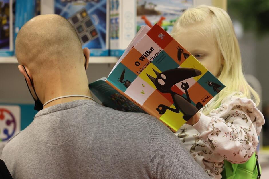 mężczyna trzymający na rękach małą dziewczynkę, która przegląda książkę