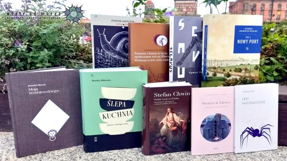Okładki 10 nominowanych książek. Są sfotografowane na tle pejzażu Gdańska
