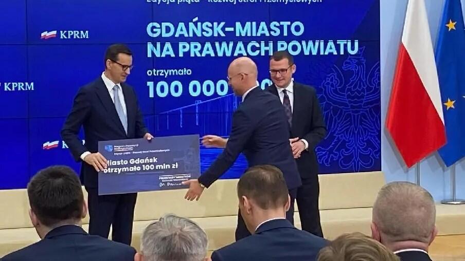 Premier Mateusz Morawiecki (po lewej) przekazuje symboliczny czek na 100 mln złotych