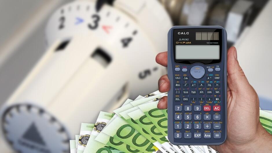 na zdjęciu kalkulator, rozłożony wachlarz pieniędzy i kaloryfer